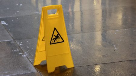 Ein gelbes Warnschild, das vor Rutschgefahr warnt, steht auf nassen Fliesen im Außenbereich