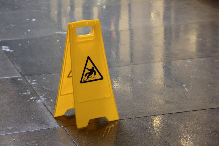 Ein gelbes Warnschild, das vor Rutschgefahr warnt, steht auf nassen Fliesen im Außenbereich