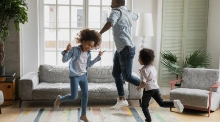 Vater springt mit seinen zwei Kindern tanzend im Wohnzimmer herum