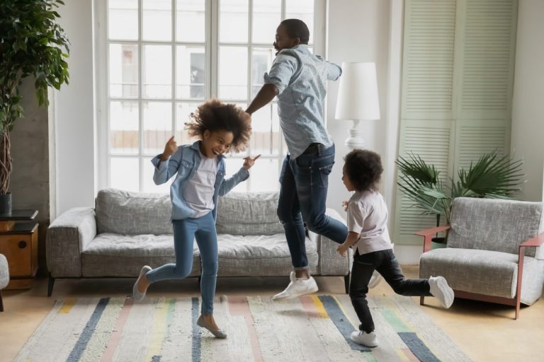 Vater springt mit seinen zwei Kindern tanzend im Wohnzimmer herum