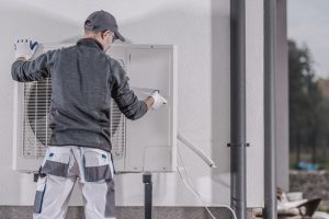 Heizungsbuaer installiert Außengerät einer Wärmepumpe an einer Gebäudewand im Rahmen einer Heizungsmodernisierung.