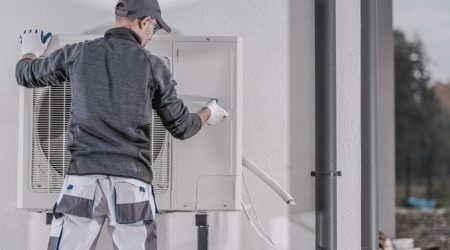 Heizungsbuaer installiert Außengerät einer Wärmepumpe an einer Gebäudewand im Rahmen einer Heizungsmodernisierung.