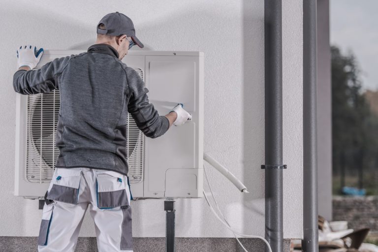 Heizungsbuaer installiert Außengerät einer Wärmepumpe an einer Gebäudewand im Rahmen einer Heizungsmodernisierung.