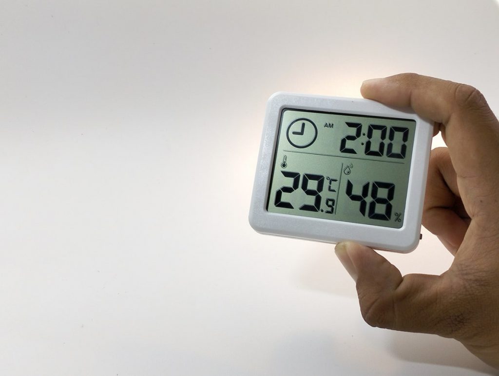 Zwei männliche Finger halten ein Hygrometer mit angezeigter Temperatur und Luftfeuchtigkeit