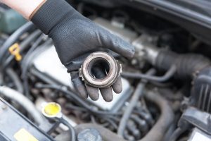 Werkstattmitarbeiter mit Handschuh hält ein defektes Ausrücklager einer Kupplung von einems Autos in der Hand