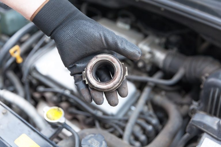 Werkstattmitarbeiter mit Handschuh hält ein defektes Ausrücklager einer Kupplung von einems Autos in der Hand