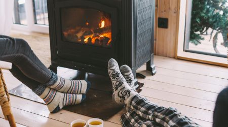 Füße von einem Pärchen mit warmen Socken vor einem brennenden Kaminofen