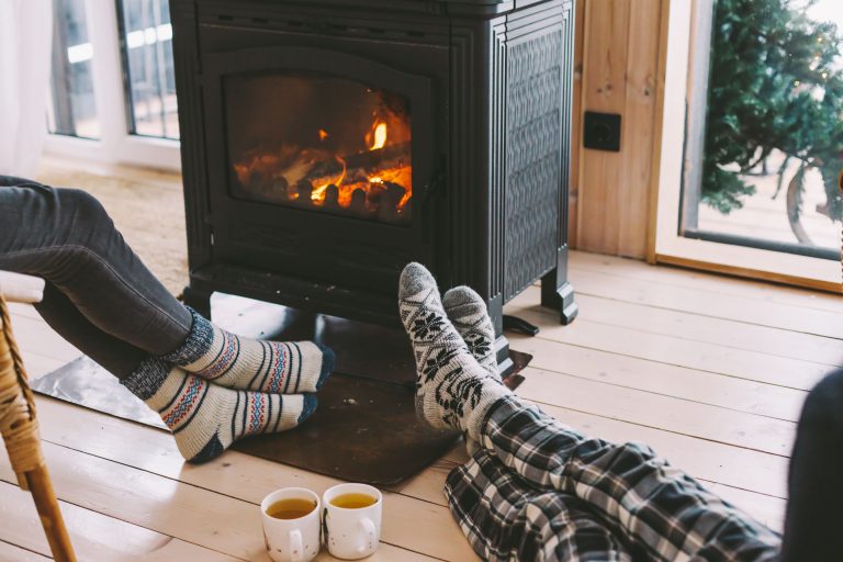 Füße von einem Pärchen mit warmen Socken vor einem brennenden Kaminofen
