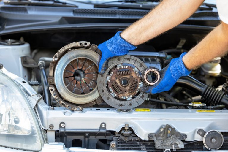 Automechaniker hält eine Kupplungsscheibe vor einem Motor eines Autos