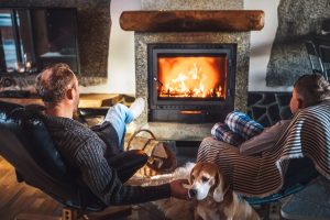 Vater sitzt mit Hund und seinem Sohn vor einem brennenden Kamin in Sesseln