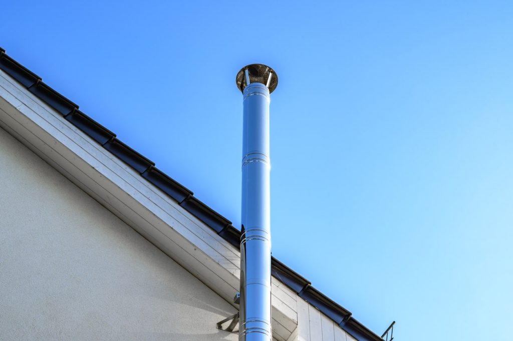 Edelstahlschornstein außen an einem Haus mit blauem Himmel im Hintergrund