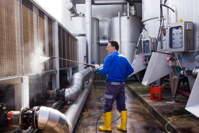 Gebäudereiniger reinigt bei einer Industriereinigung Maschinen mit einem Dampfstrahler