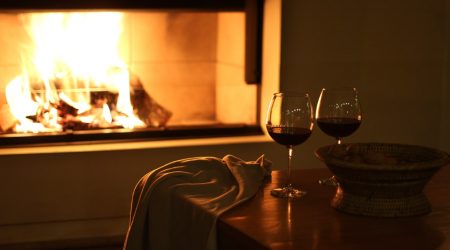 Weingläser mit Rotwein vor einem offenen Kamin