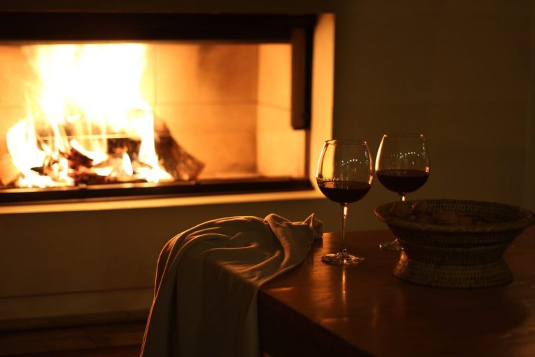 Weingläser mit Rotwein vor einem offenen Kamin