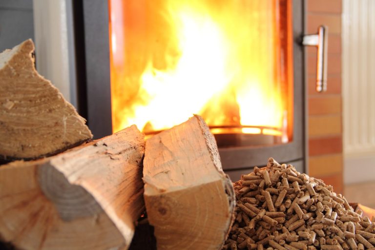 Brennender Kaminofen mit Holzscheit und Pellets im Vordergrund