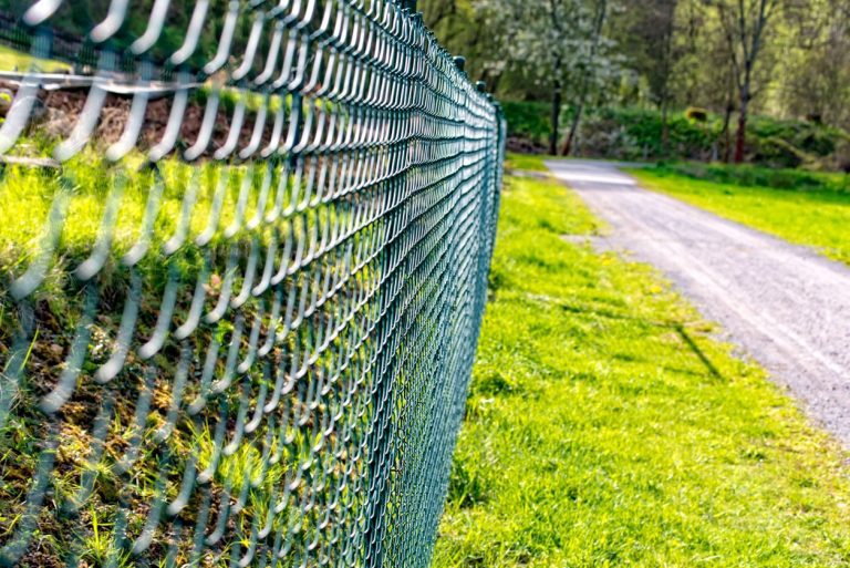 Grüner Maschendrahtzazn an einem Schotterweg mit grünem Rasen