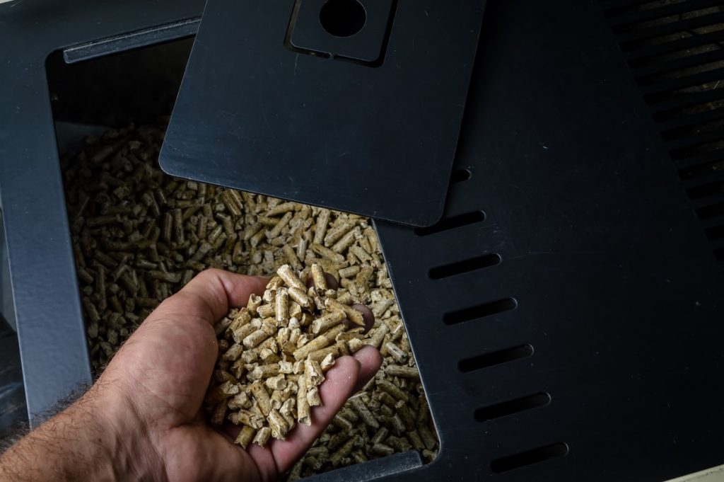 Ein Mann nimmt Pellets aus einem schwarzen Pelletofen in die Hand