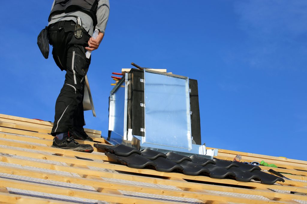 Handwerker auf einem abgedeckten Dach baut einen Schornstein aus Edelstahl