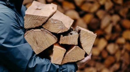 Mann trägt geschlichtetes Brennholz in Armen