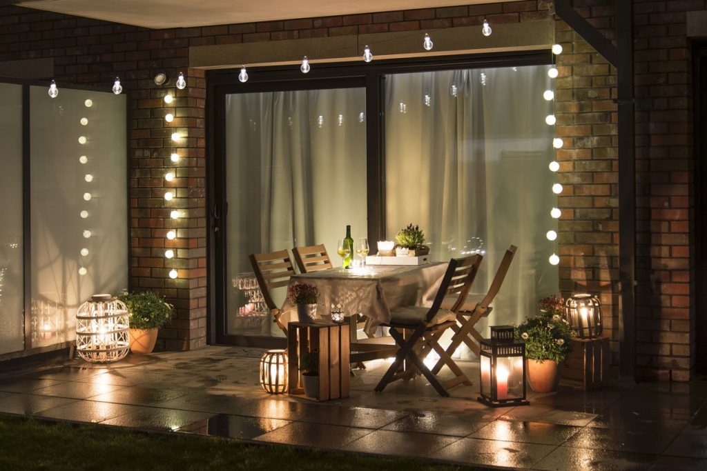 Eine gemütlich beleuchtete Terrasse mit unterschiedlichen Lichtquellen und einem Tisch mit zwei Weingläsern
