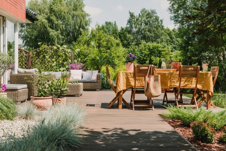 Esstischgruppe auf einer großen Holzterrasse mit Sitzgruppe im Hintergrund