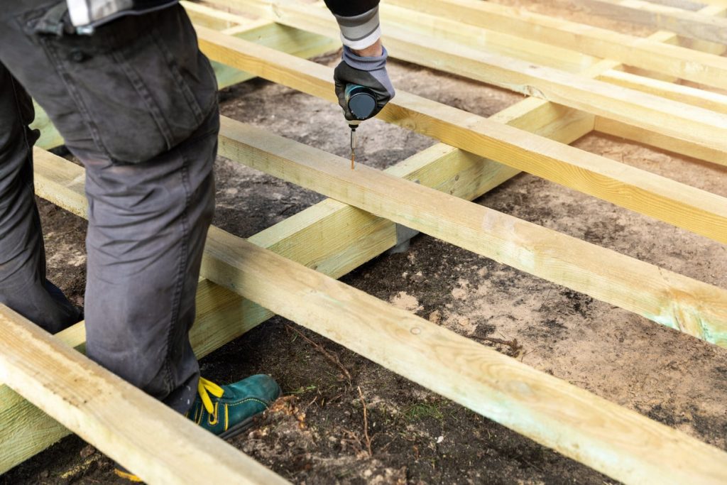 Handwerker verschraubt die Unterkonstruktion aus Holz einer Terrasse mit einem Akkuschrauber