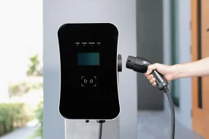Eine Hand führt einen Ladestecker für E-Autos in eine an der Garagenwand installierten Wallbox