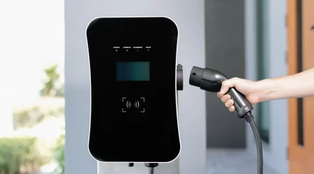 Eine Hand führt einen Ladestecker für E-Autos in eine an der Garagenwand installierten Wallbox