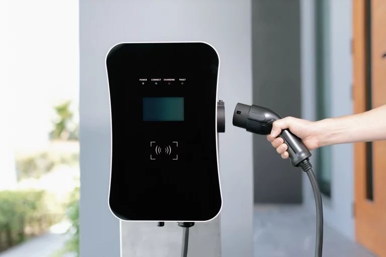 Eine Hand führt einen Ladestecker für E-Autos in eine an der Garagenwand installierten Wallbox