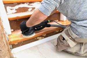 Tischler schleift mit einem Schwingschleifer eine alte Holztreppe ab