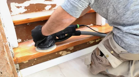 Tischler schleift mit einem Schwingschleifer eine alte Holztreppe ab