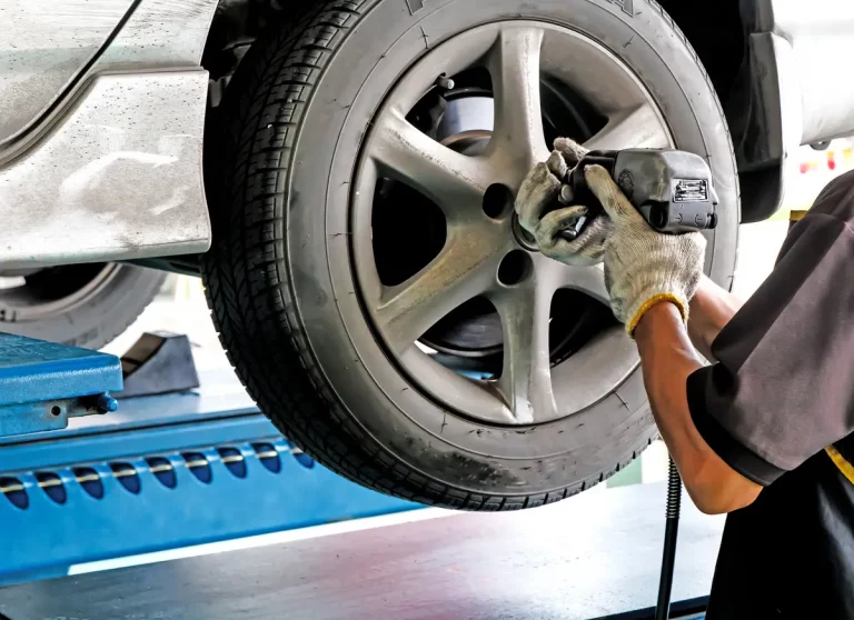 KFZ Mechaniker wechselt Reifen bei einem Auto in einer Werkstatt