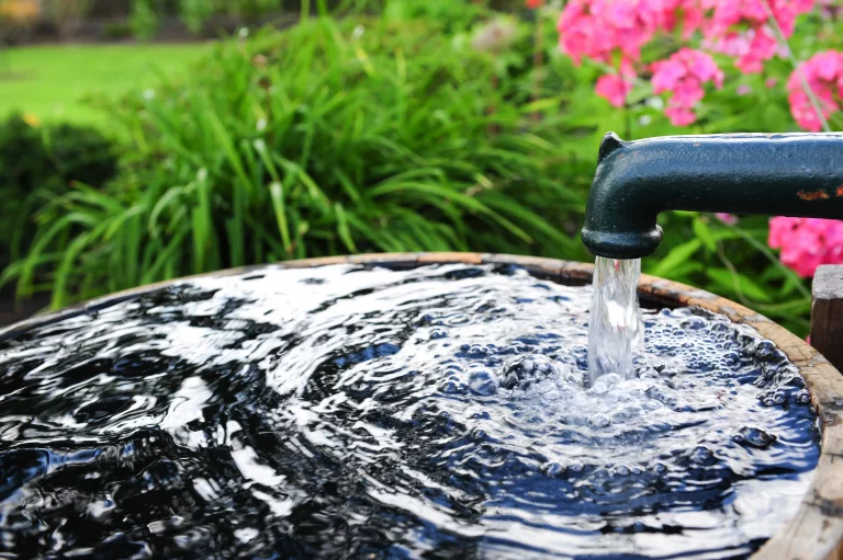 Nahaufnahme eines Grundwasserbrunnens. Wasser fliest aus dem Hahn des Brunnens in ein Auffangbecken