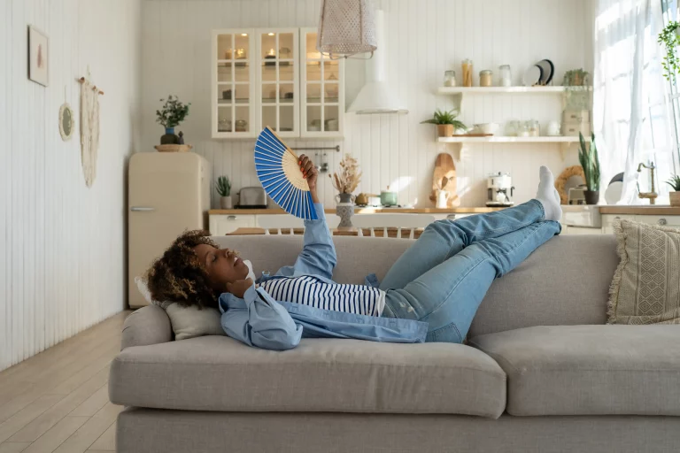 Junge Frau mit Hitzewallungen, die sich während der Hitzewelle in einer Wohnung ohne Klimaanlage heiß fühlt
