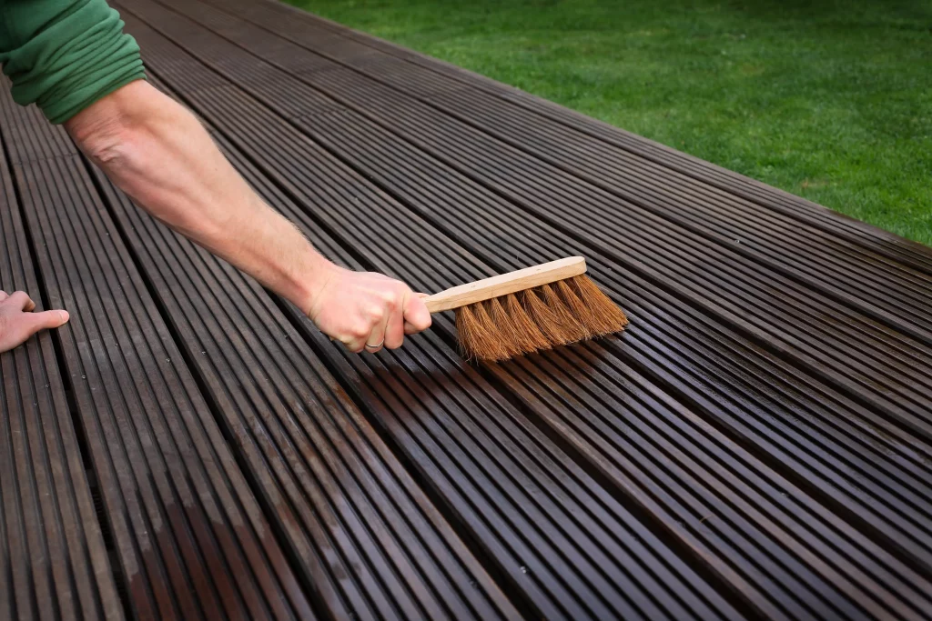 Hand mit einem Besen kehrt über eine Holzterrasse