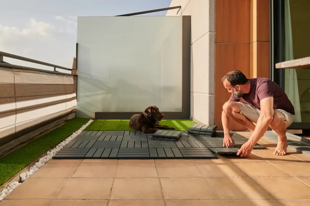 Ein Hund beobachtet einen Mann beim Verlegen von WPC Platten auf dem eigenen Balkon