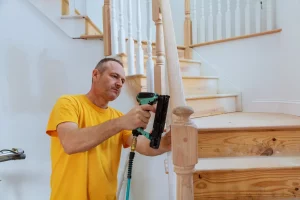 Schreiner montiert mit einer elektrischen Nagelpistole ein neues Treppengeländer aus Holz