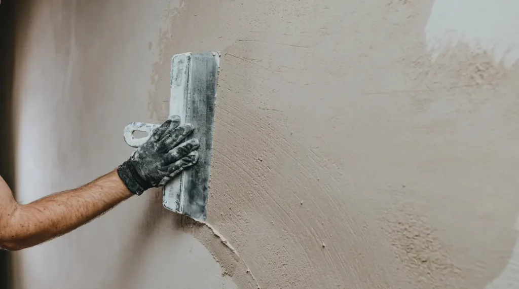 Maler im Arbeitsoverall verputzt eine Wand mit einer Putzspachtel