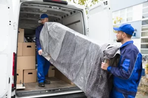 Zwei Mitarbeiter einer Möbelspedition heben ein verpacktes Sofa in einen Transporter