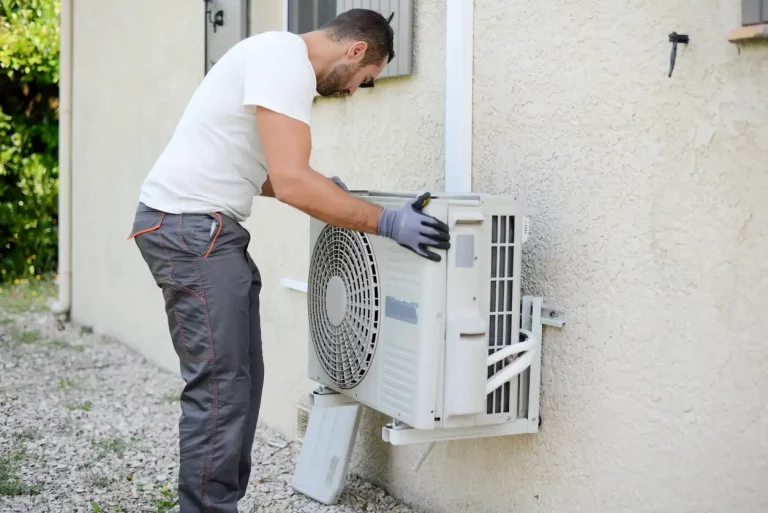 Klimatechniker mit Handschuhen montiert eine Split-Klimaanlage an der Außenwand eines Wohnhauses.