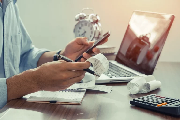 Mann hält Papierrechnungen mit Taschenrechner zur Berechnung von Mehrwertsteuer
