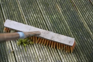 Besen schrubbt über eine alte vermooste Holzterrasse