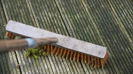 Besen schrubbt über eine alte vermooste Holzterrasse