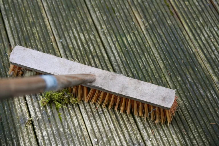 Besen schrubbt über eine alte vermooste Holzterrasse