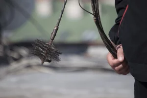 Nahaufnahme eines Schornsteinfegers bei der Arbeit, der eine Kette mit Besen in der Hand hält