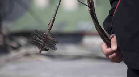 Nahaufnahme eines Schornsteinfegers bei der Arbeit, der eine Kette mit Besen in der Hand hält