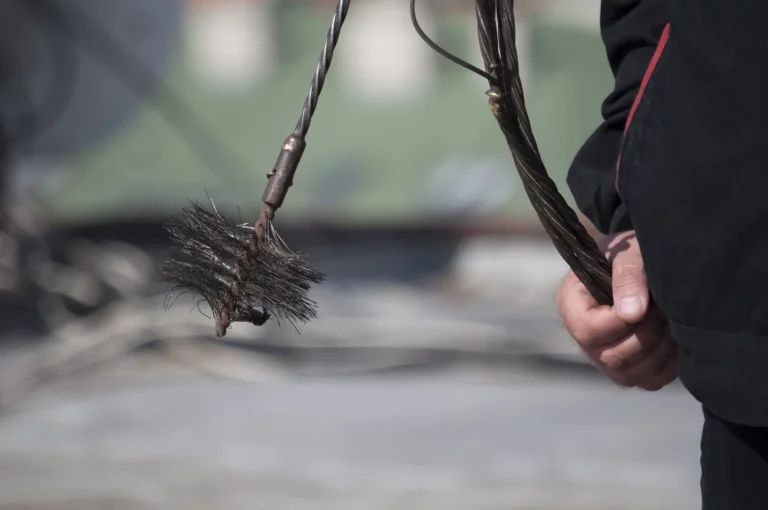 Nahaufnahme eines Schornsteinfegers bei der Arbeit, der eine Kette mit Besen in der Hand hält