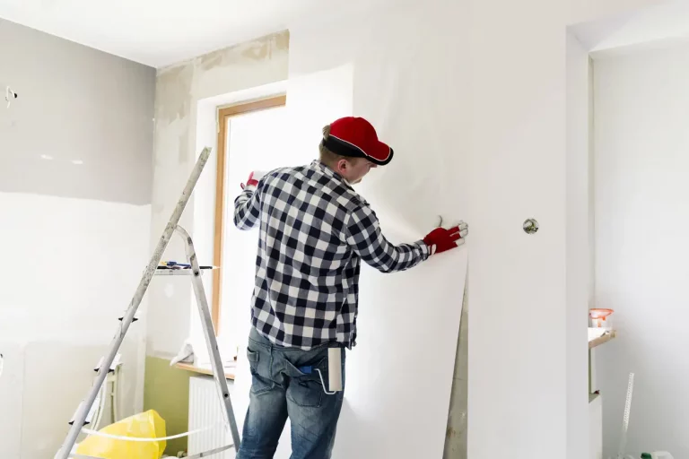 Maler bringt beim Tapezieren einer Wohnung Tapete an eine Wand an