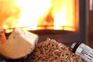 Ein Holzscheit und Pellets mit einem Heizthermostat vor einem brennenden Kaminofen