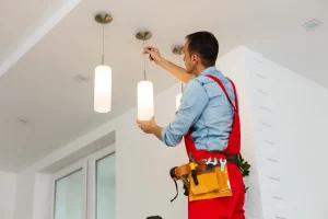 Elektriker in roter Arbeitshose montiert hängende Lampen an einer Decke in einer Wohnung